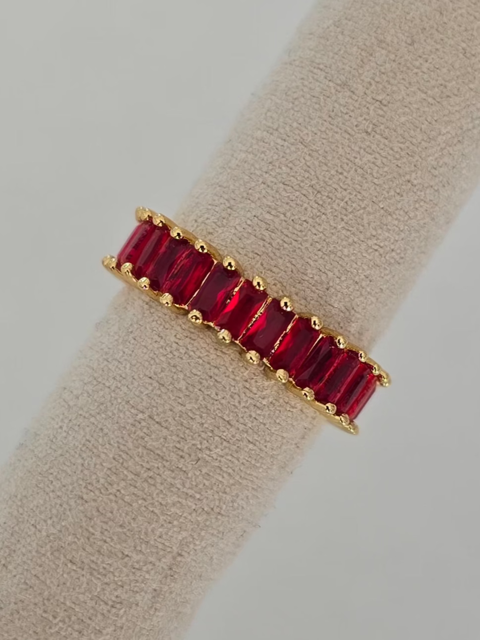 bague dorée Lumired avec pierres rouges rectangulaire présentée sur un coussin d'exposition