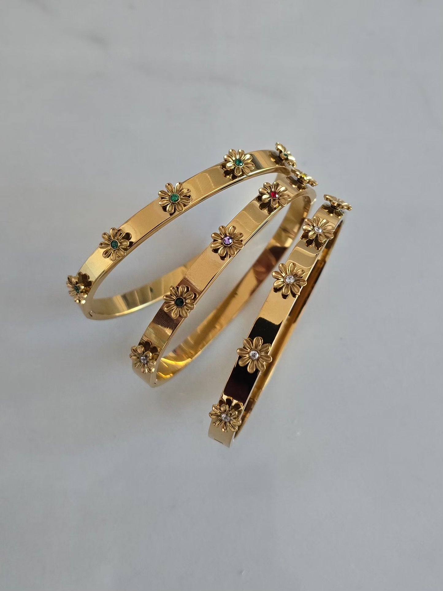 Trois bracelets joncs Margarita dorés en acier inoxydable ornés de cinq fleurs en relief 3D