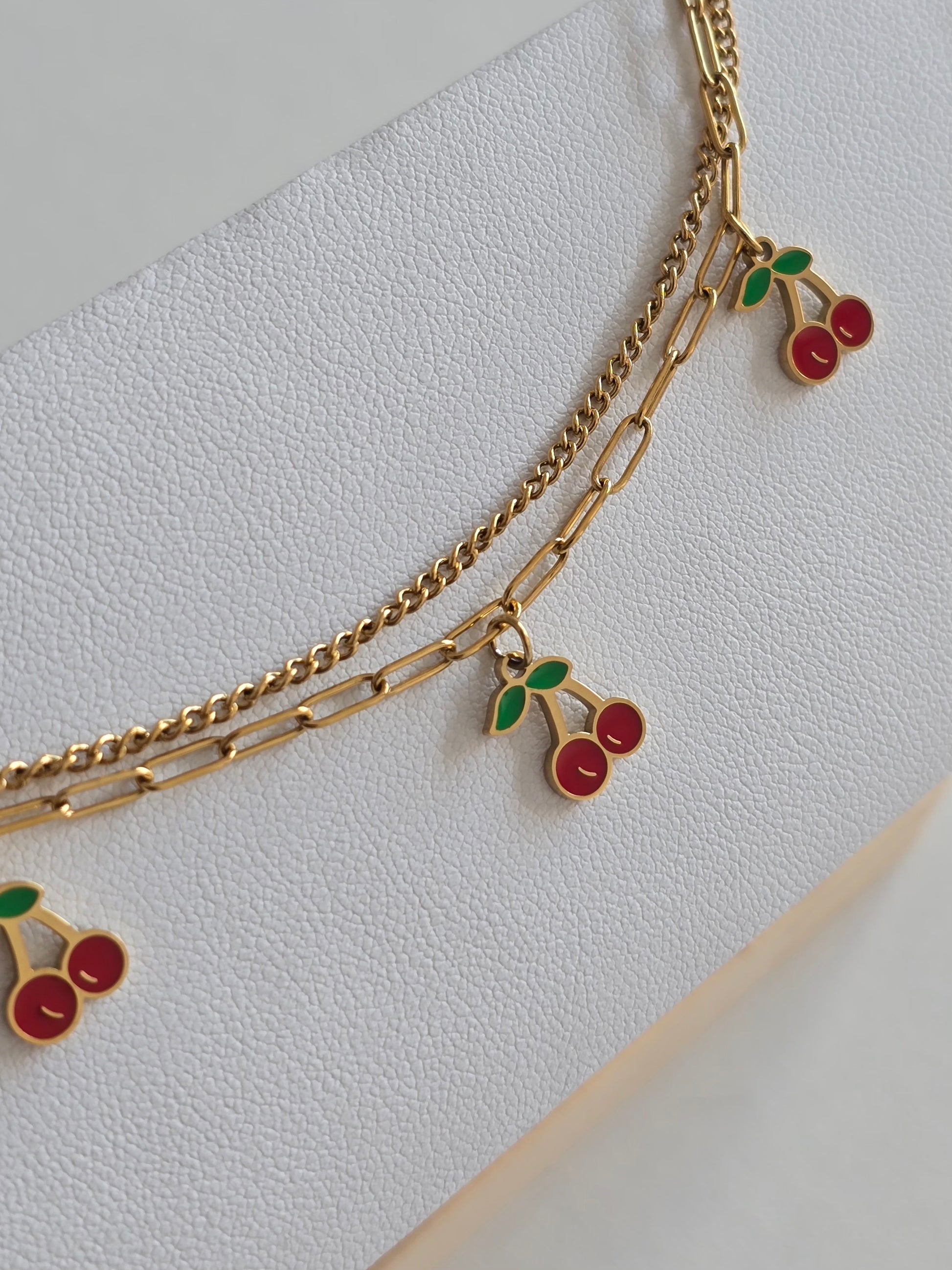 gros plan sur un bracelet de cheville doré orné de pendentifs cerises 