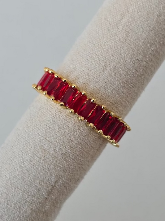 bague Lumired dorée ornée de pierres rouges brillantes posée sur support 