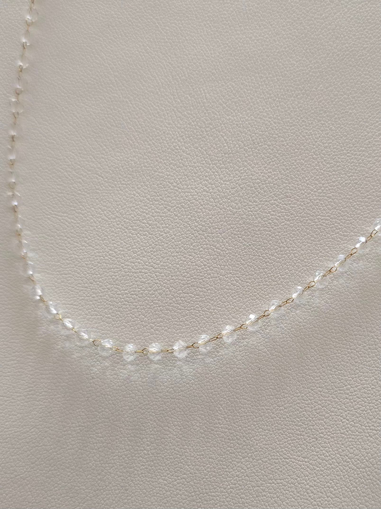 Détail du collier Clarity avec chaîne dorée et perles transparentes 