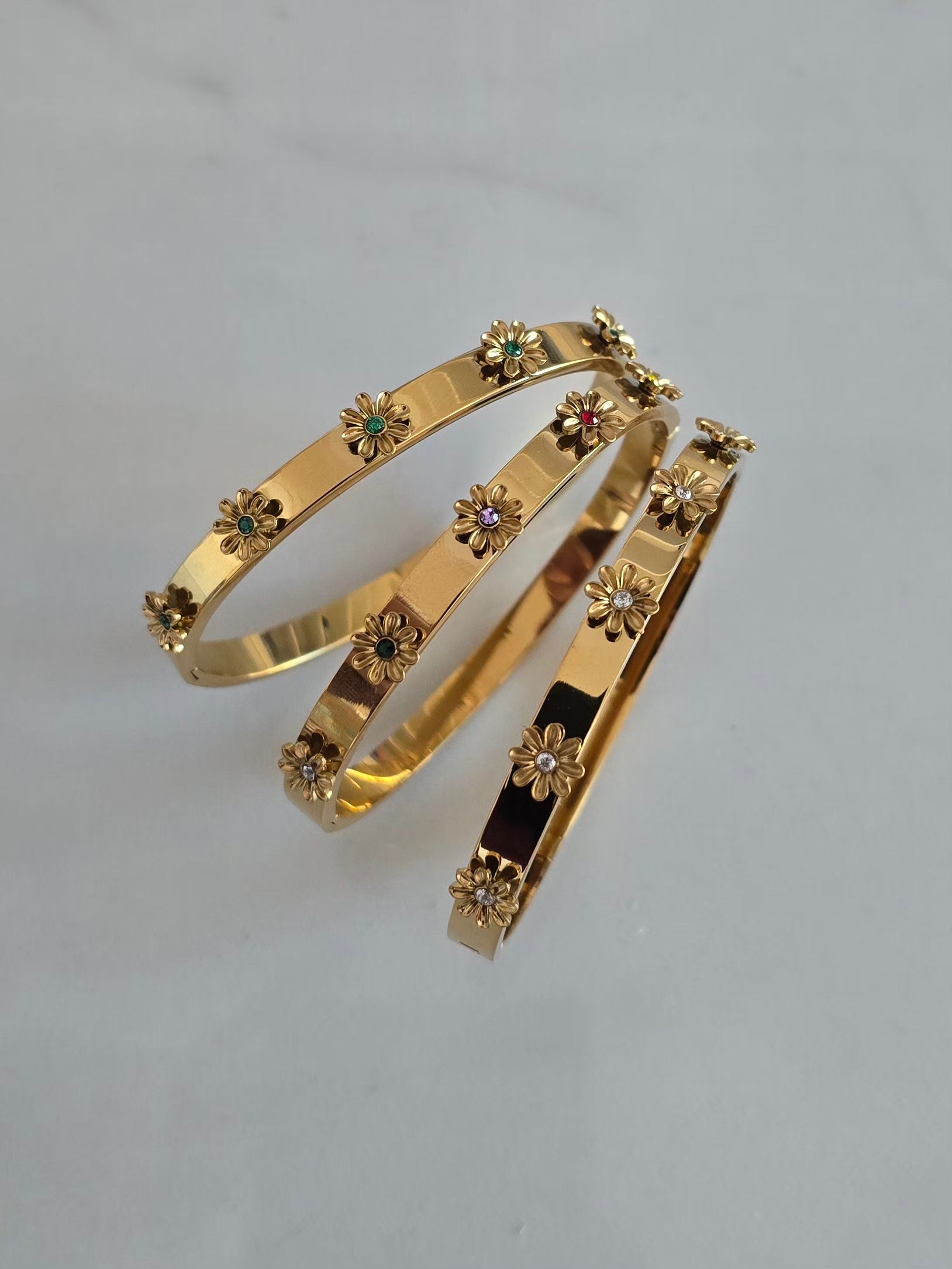 Trois bracelets joncs Margarita dorés en acier inoxydable ornés de cinq fleurs en relief 3D