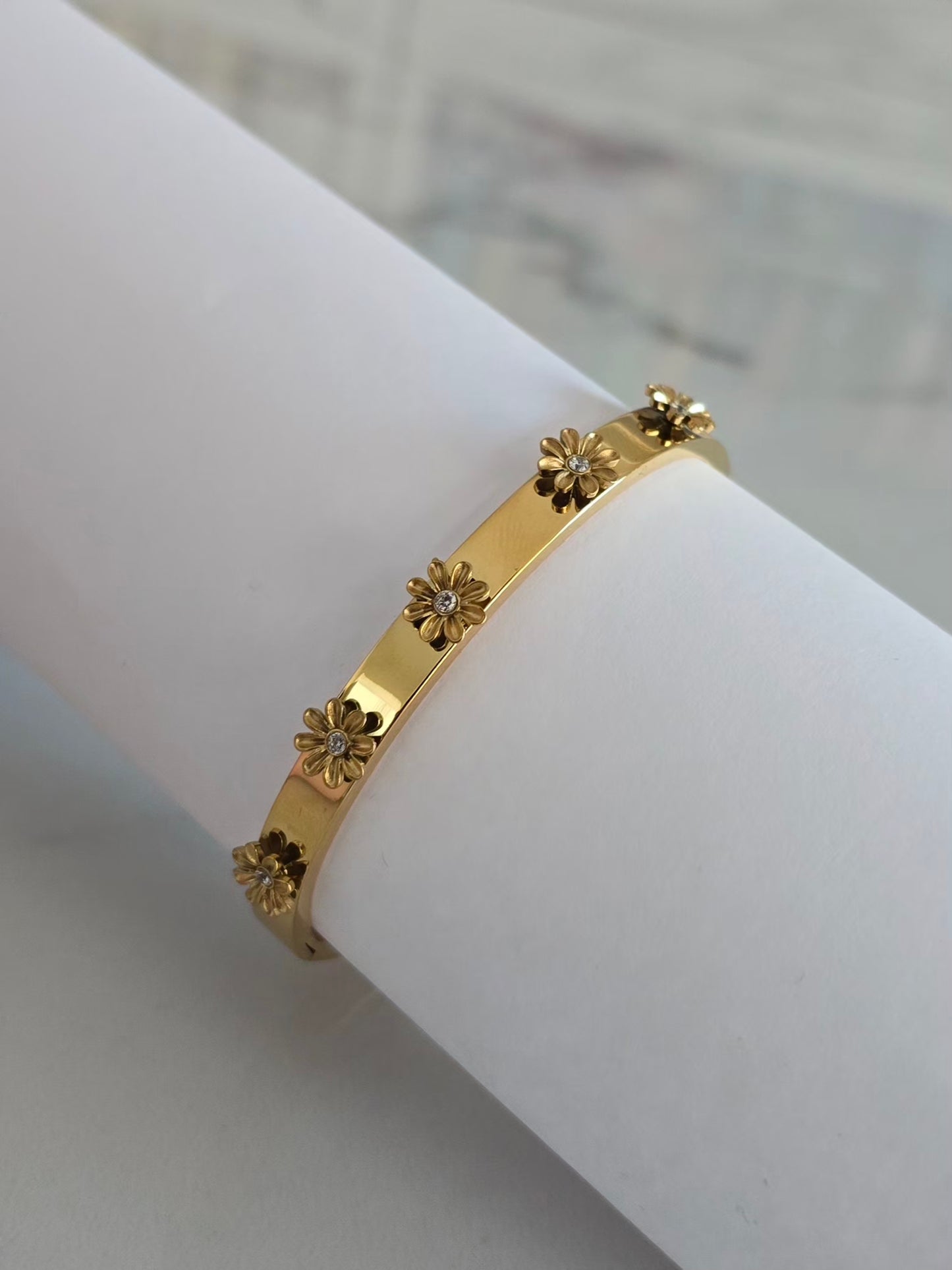 Bracelet jonc Margarita doré avec cinq fleurs en relief 3D serties de détails blancs brillants.