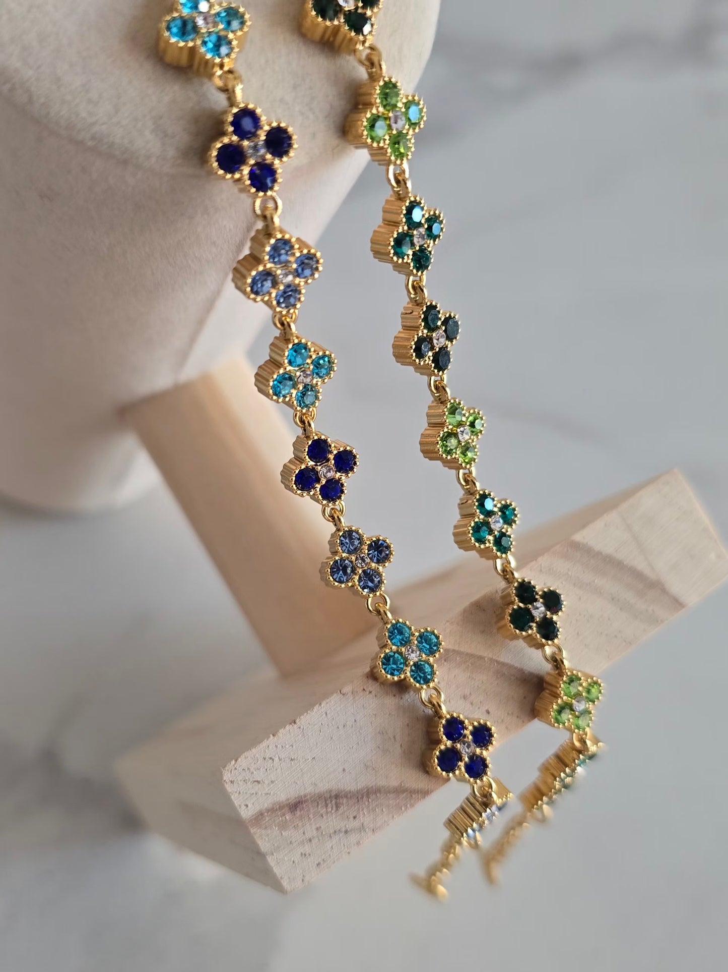 Bracelets Princesa dorés suspendus sur présentoir, ornés de délicates fleurs à strass bleus et verts