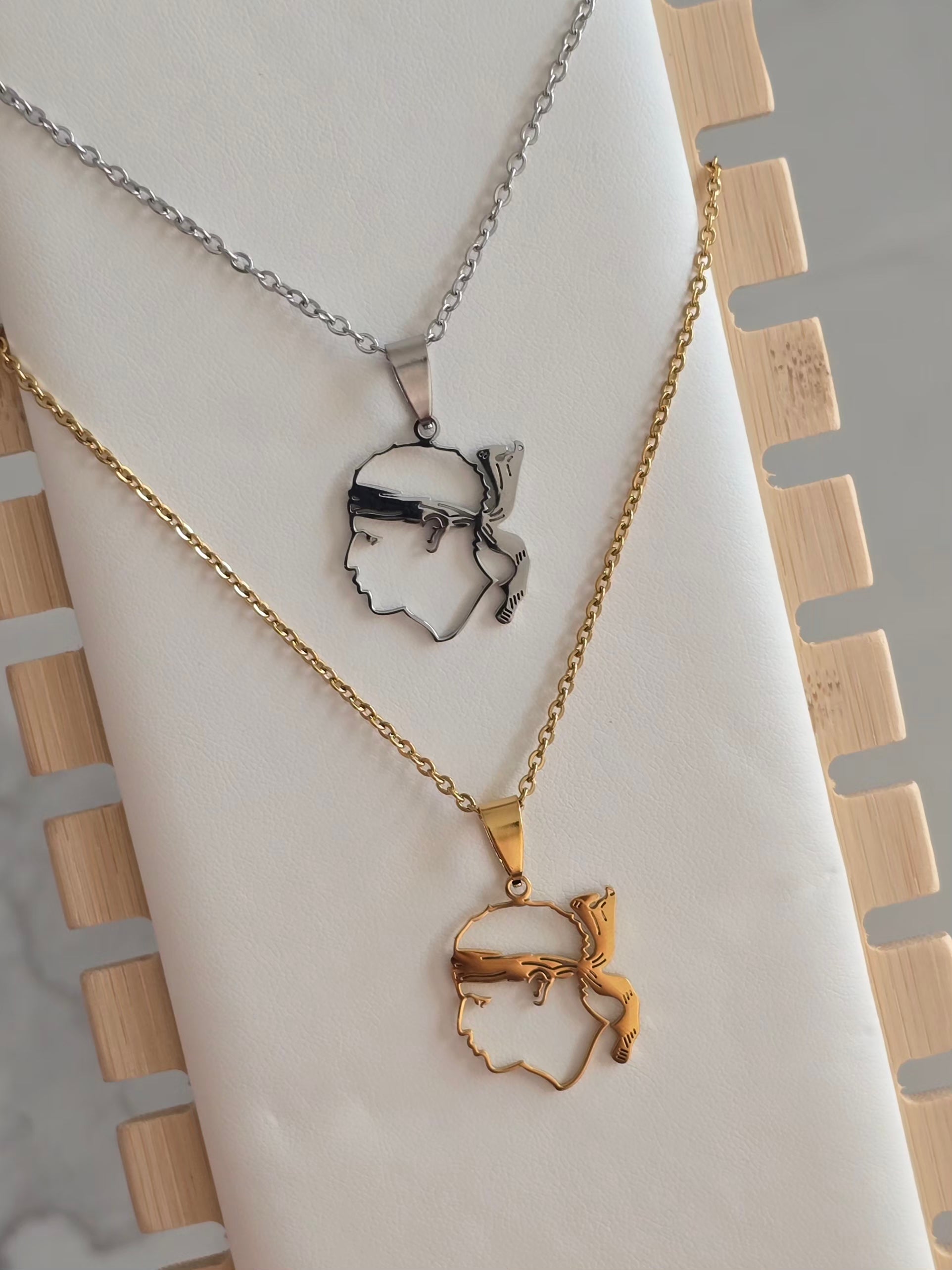 Colliers Testa Mora contour doré et argenté en acier inoxydable présentés sur support à bijoux. 